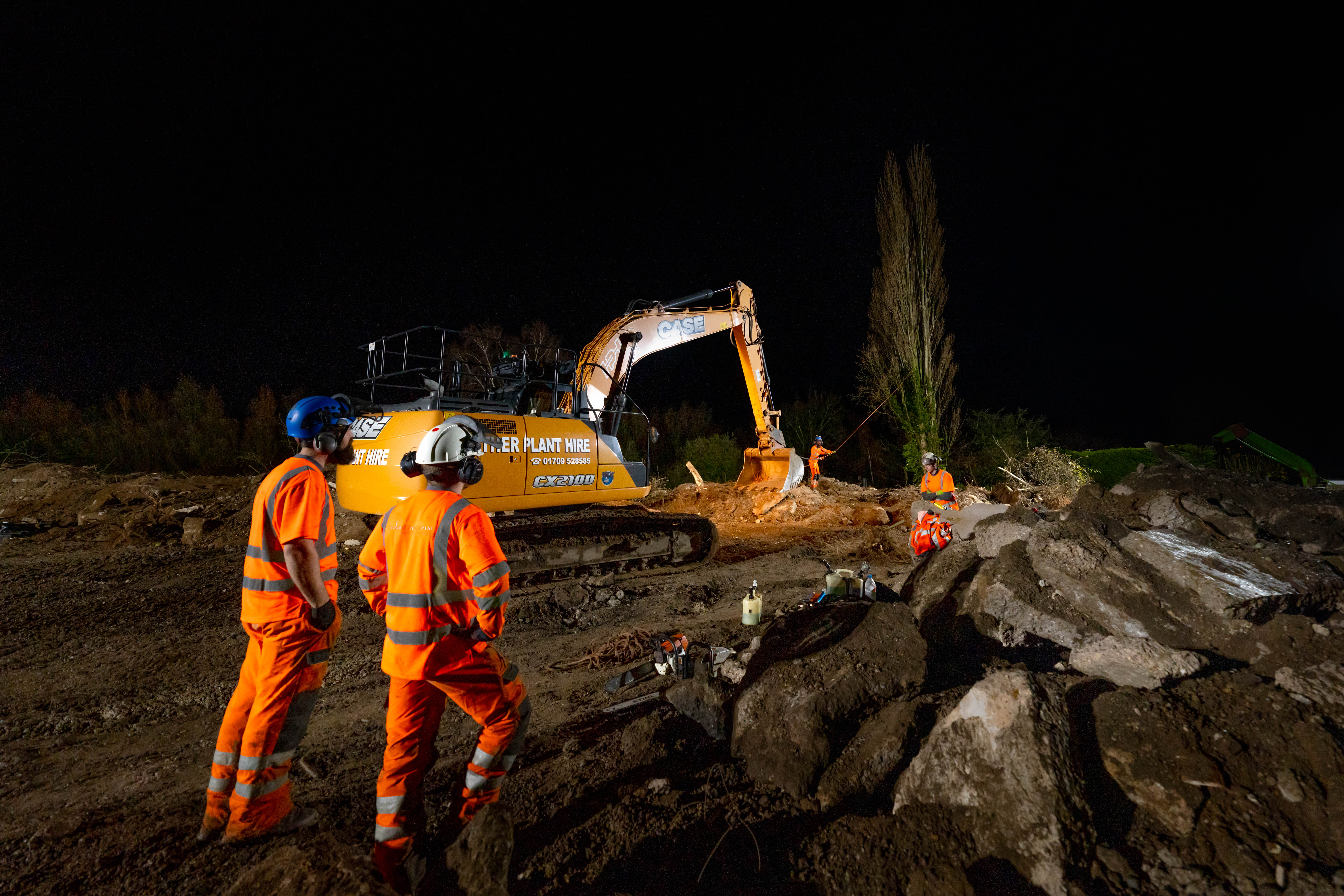 Team of groundworkers on site at night with excavator 