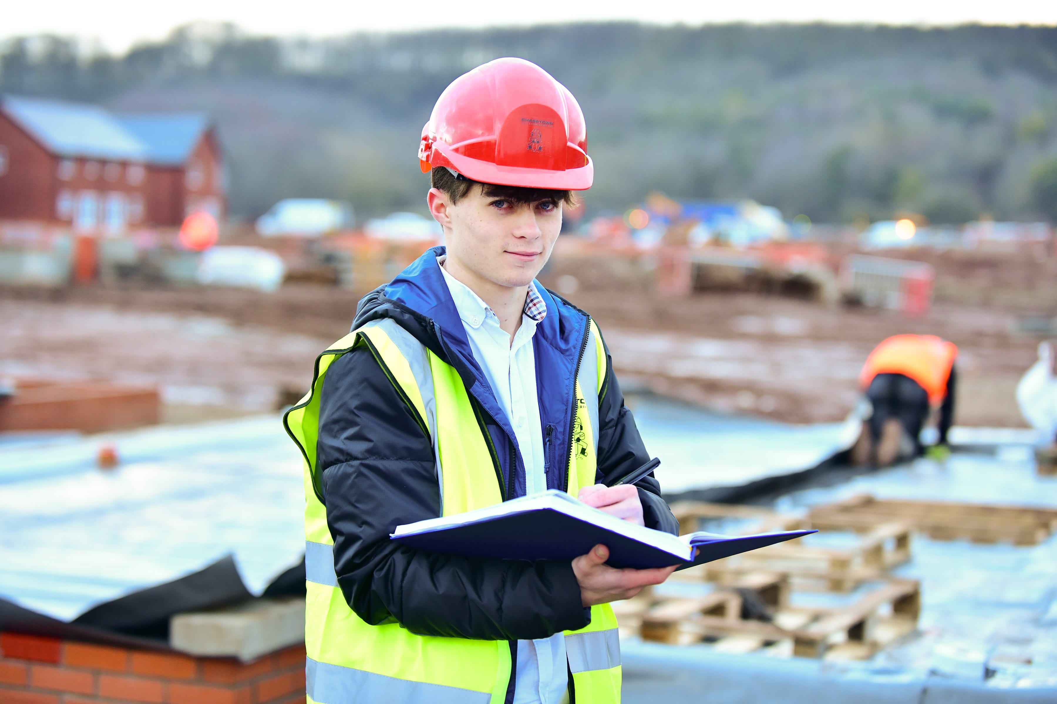 Young student on site with hard hat and clipboard 