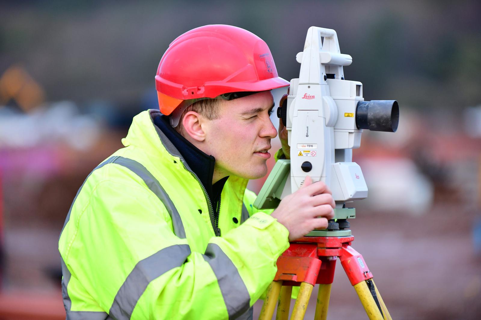 Young groundworker on site with automatic level 